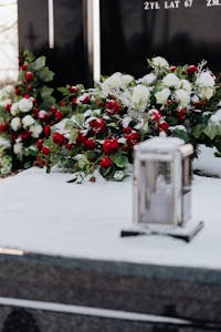A snowy grave adorned with red and white floral wreaths and a lit candle in winter.