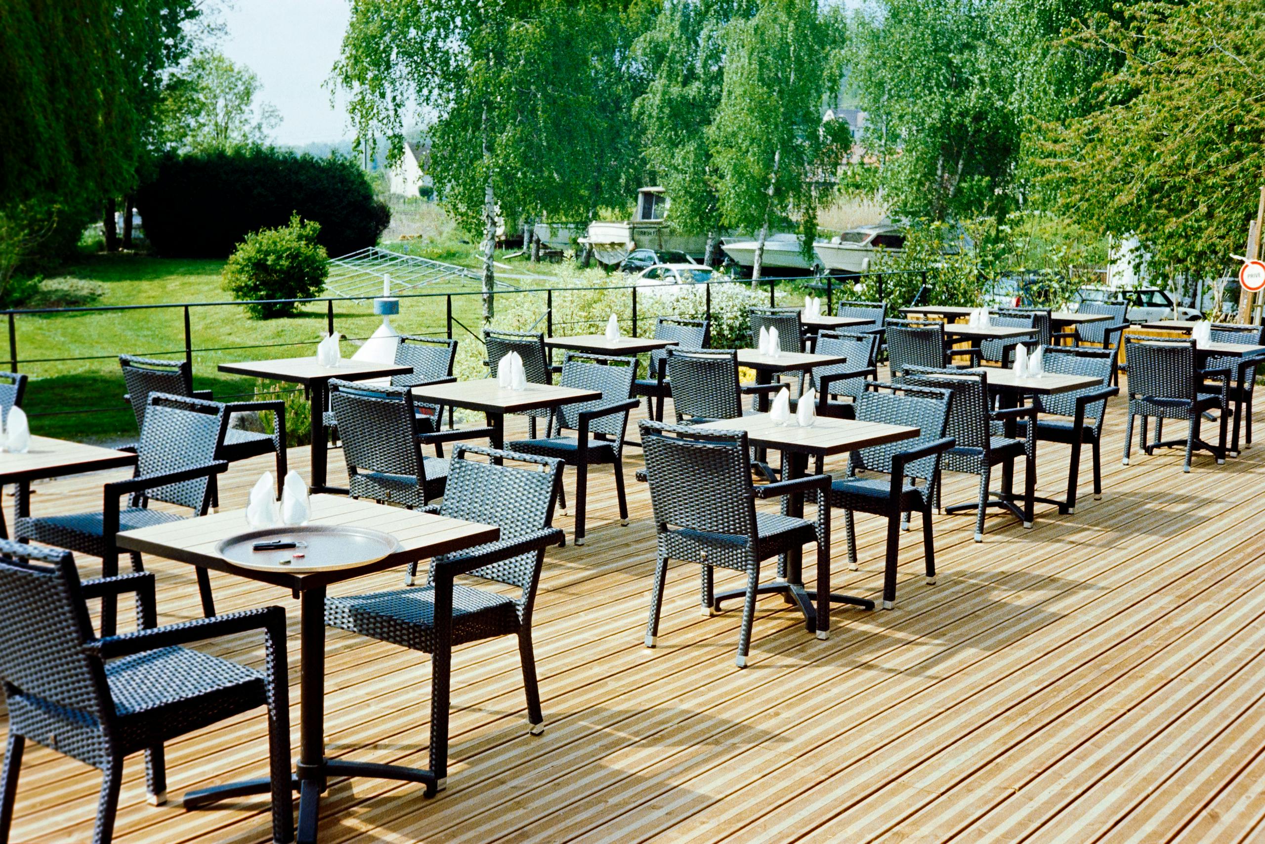 Peaceful view of an empty outdoor café terrace in Hauts-de-France, France, with wicker furniture and lush greenery.