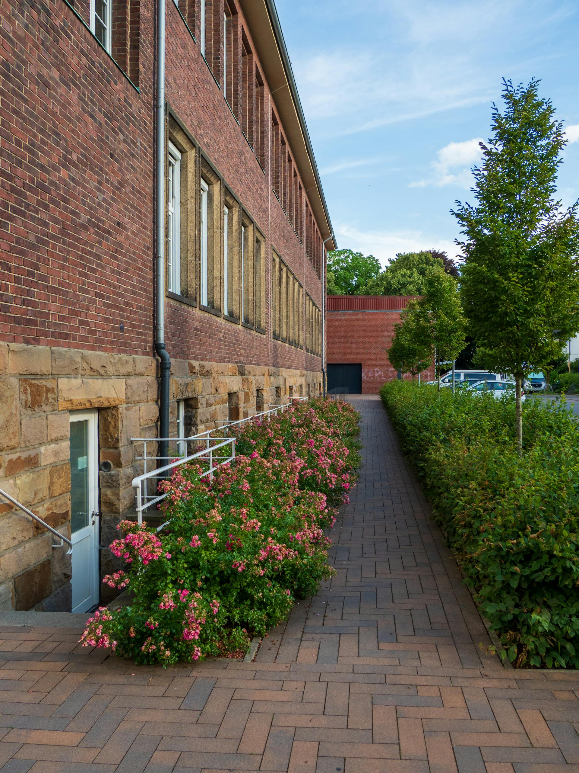 Red brick building exterior with lush garden path and blooming flowers.